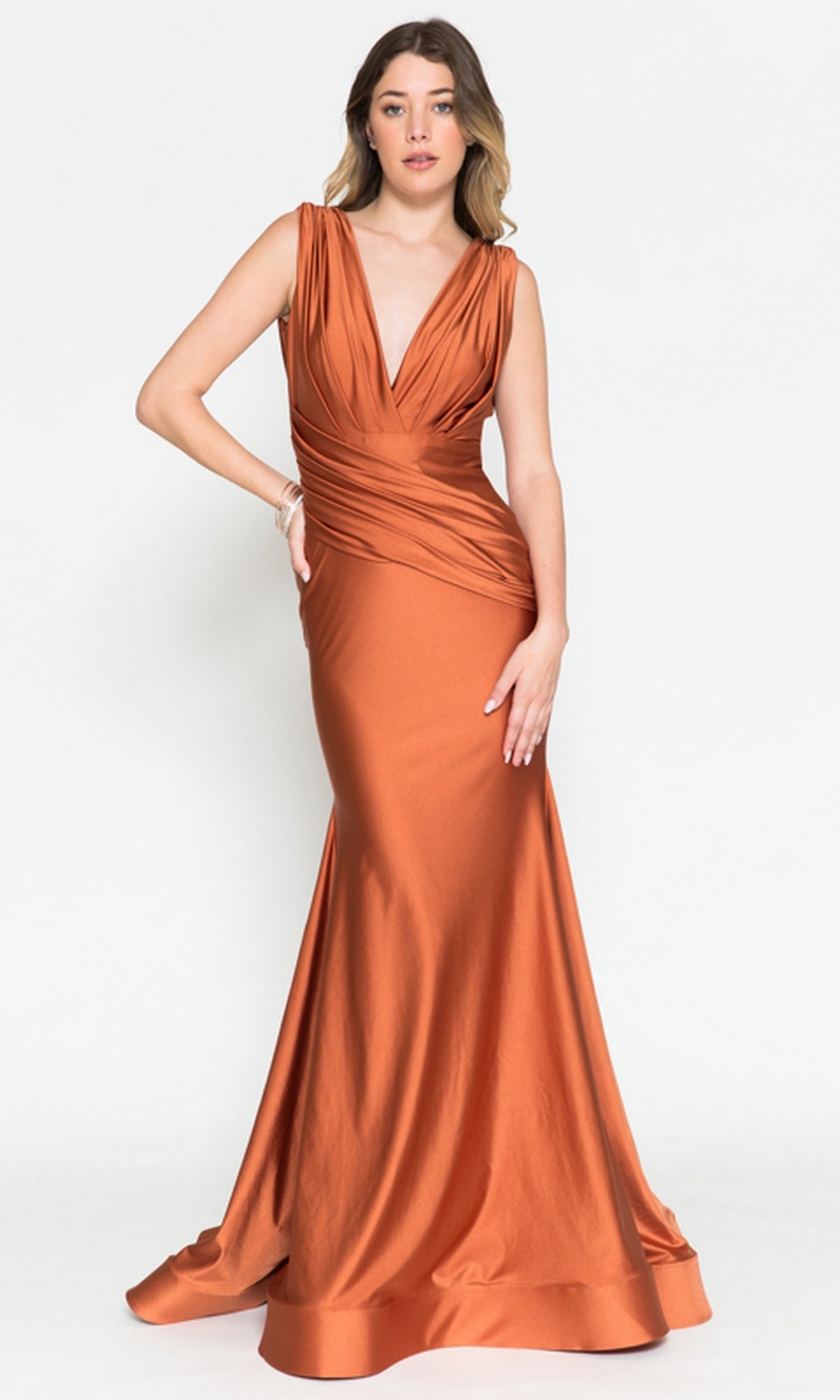 A woman stands against a plain white background in the Amelia Couture 370 Plunging V-Neck Long Lycra Prom Dress, a sleeveless, floor-length mermaid gown in rust with a deep V-neckline.
